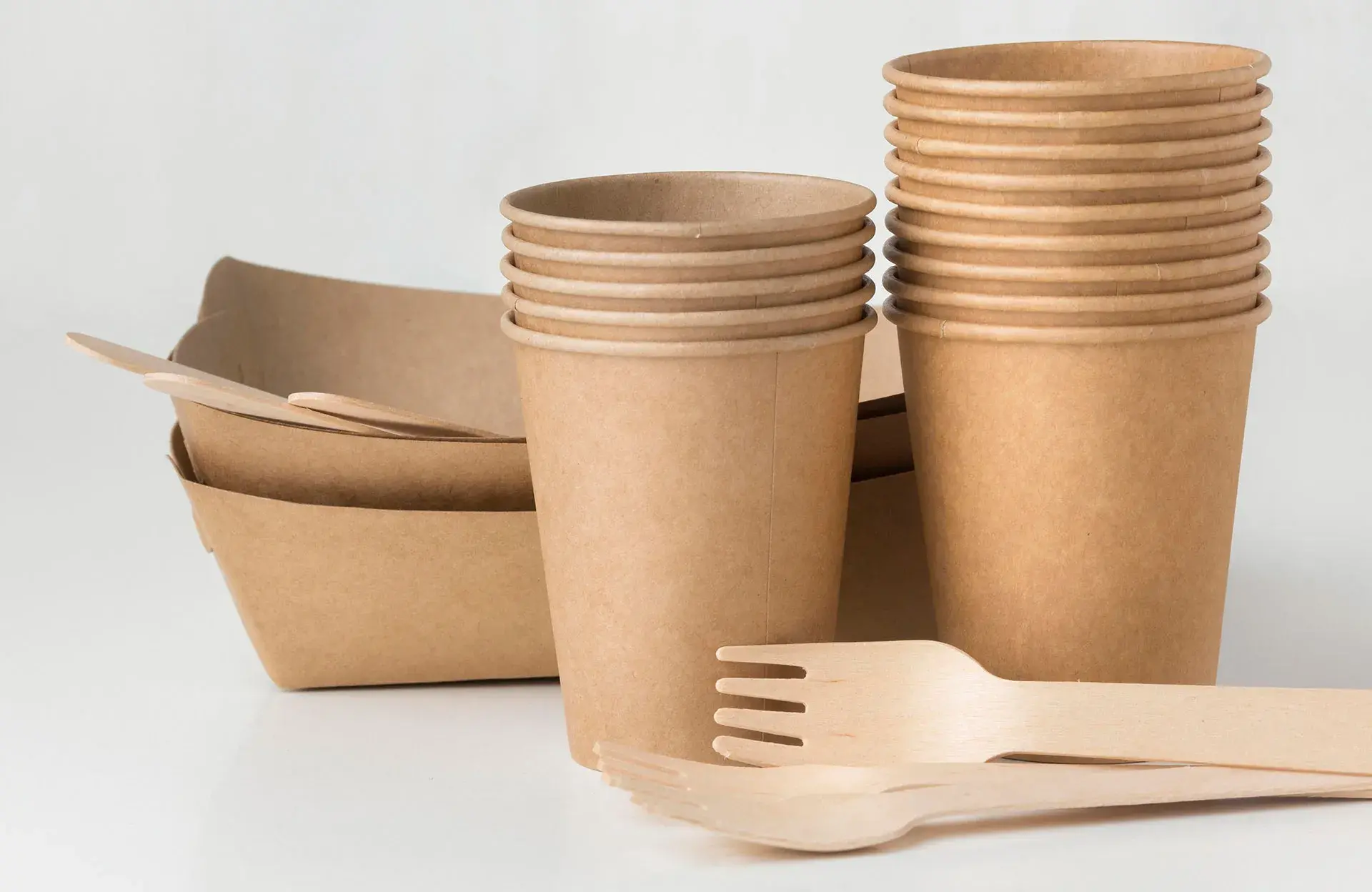 Vasos desechables ecológicos de cartón y cubiertos de madera para branding sustentable.